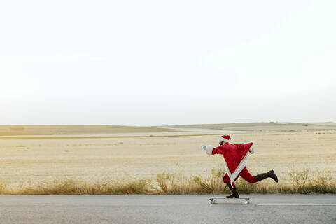 Weihnachtsmann fährt auf Longboard auf Landstraße, lizenzfreies Stockfoto