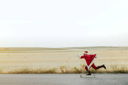 Weihnachtsmann fährt auf Longboard auf Landstraße - JCMF00175