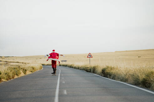 Weihnachtsmann fährt auf Longboard auf Landstraße - JCMF00176