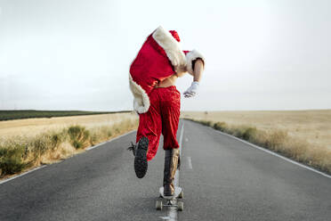 Santa Claus riding on longboard on country road - JCMF00177