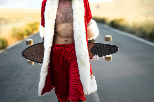 Mittelteil des Weihnachtsmanns mit einem Longboard auf der Landstraße - JCMF00180