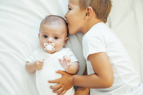 Older brother kissing baby boy in bed stock photo