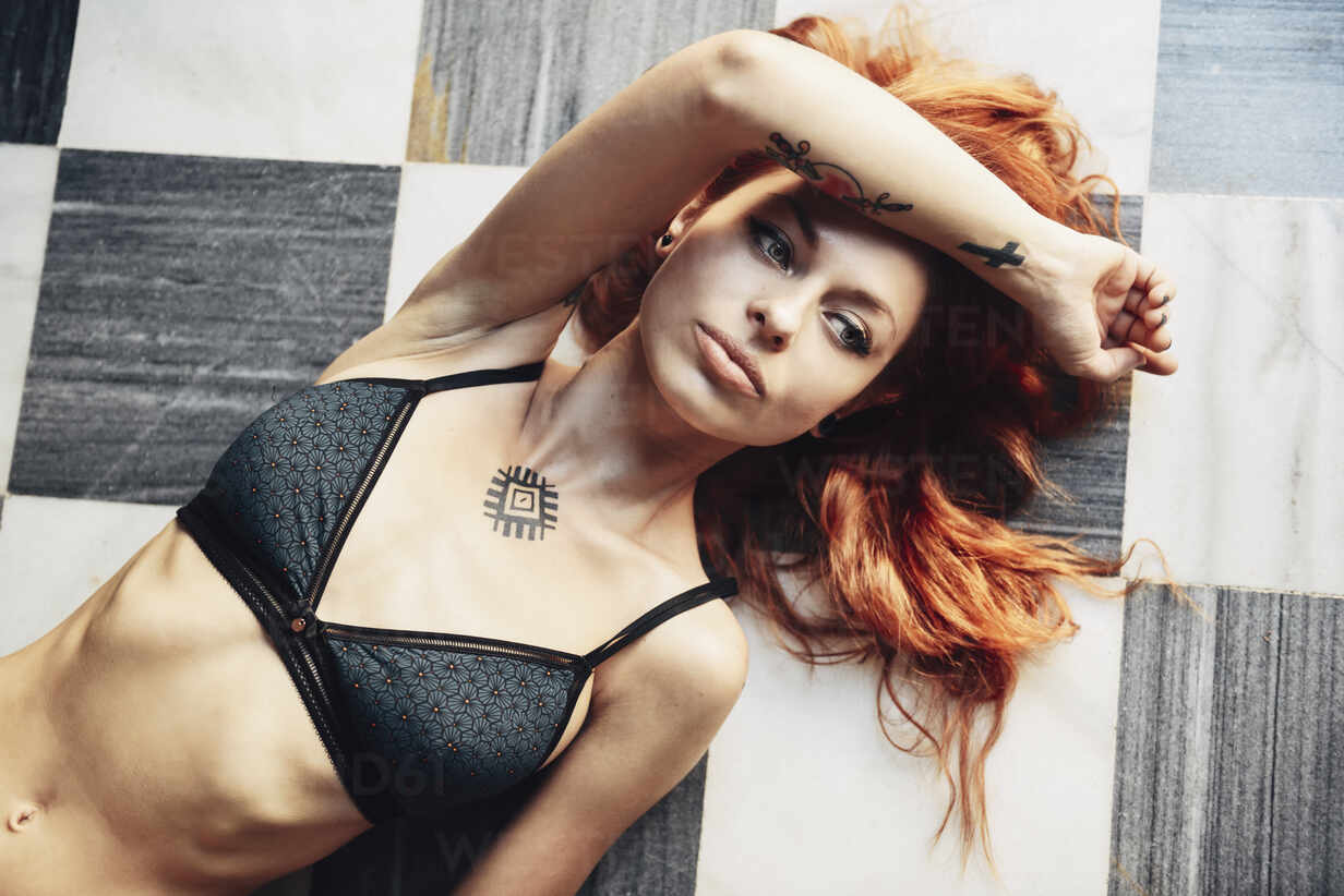 Red-haired tattooed woman in lingerie lying on a black and white checkered  floor stock photo