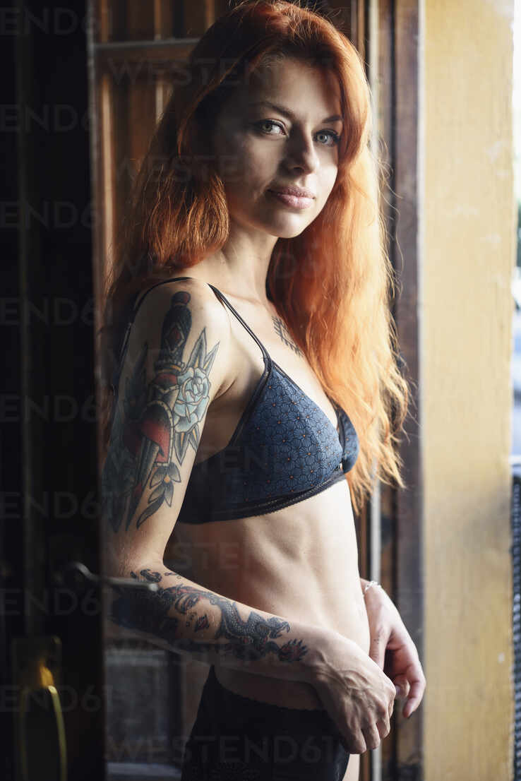 Red-haired tattooed woman in lingerie at home near the window stock photo