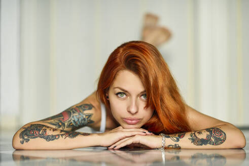 Red-haired tattooed woman in lingerie at home near the window