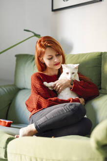 Rothaarige Frau mit Katze auf der Couch zu Hause - JSMF01261