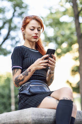 Porträt einer rothaarigen, tätowierten Frau, die im Freien ein Mobiltelefon benutzt, lizenzfreies Stockfoto