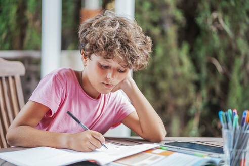 Boy sitting at garden table doing homework - DLTSF00079