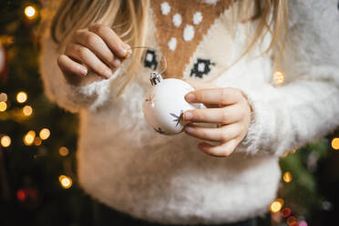 Schmücken des Weihnachtsbaums, Mädchen hält eine weiße Christbaumkugel mit silbernen Sternen - IPF00523