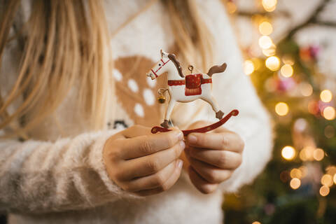 Schmücken des Weihnachtsbaums, Mädchen hält ein ornamentales Metallschaukelpferd, lizenzfreies Stockfoto