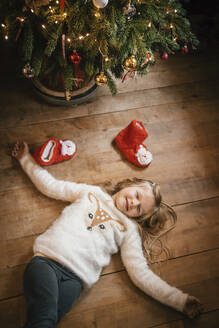 Lächelndes Mädchen mit geschlossenen Augen unter dem Weihnachtsbaum liegend - IPF00527