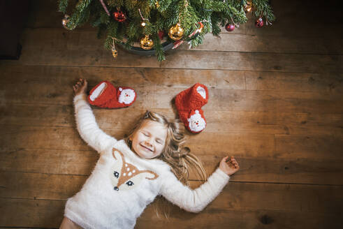 Smiling girl with closed eyes lying under the Christmas tree - IPF00529