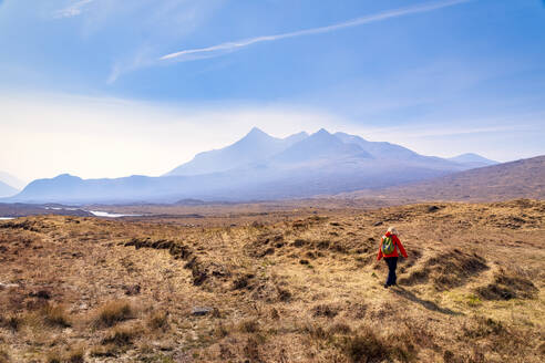 Rückansicht einer reifen Frau, die auf dem Land spazieren geht, mit den Cuillin-Bergen im Hintergrund, Isle of Skye, Highlands, Schottland, UK - SMAF01502