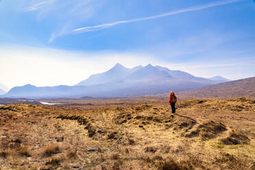 Ältere Frau, die auf dem Land steht, mit den Cuillin-Bergen im Hintergrund, Isle of Skye, Highlands, Schottland, UK - SMAF01503