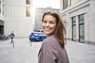 Smiling businesswoman with windswept hair in the city turning round - PNEF01868