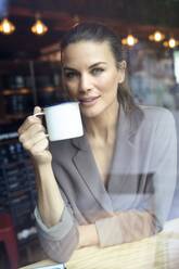Porträt einer Geschäftsfrau hinter einer Fensterscheibe in einem Café, die Kaffee trinkt - PNEF01870
