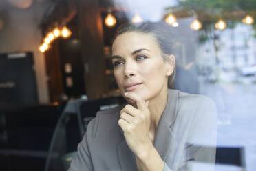 Porträt einer nachdenklichen Geschäftsfrau hinter einer Fensterscheibe in einem Café - PNEF01871