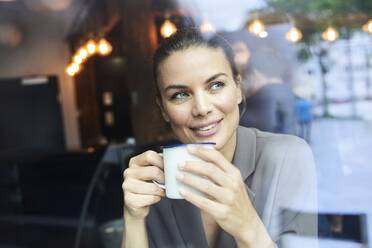 Portrait of businesswoman behind windowpane in a cafe drinking coffee - PNEF01872