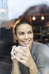 Porträt einer Geschäftsfrau hinter einer Fensterscheibe in einem Café, die Kaffee trinkt - PNEF01874