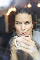 Porträt einer Geschäftsfrau hinter einer Fensterscheibe in einem Café, die Kaffee trinkt - PNEF01875