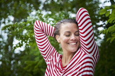 Porträt einer glücklichen Frau mit nassen Haaren und gestreiftem Oberteil in der Natur - PNEF01932