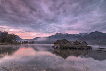 Lila Himmel bei Sonnenuntergang und Holzhütten spiegeln sich im klaren Wasser des Kochelsees, Schlehdorf, Bayern, Deutschland, Europa - RHPLF08715