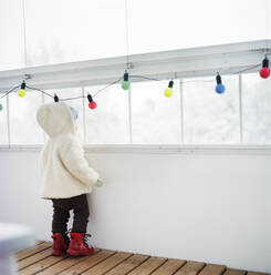 Rückansicht eines Kindes mit warmer Kleidung und Blick aus dem Fenster - FOLF10414