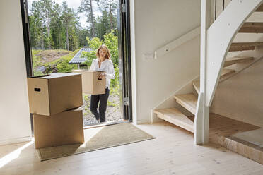 Woman carrying cardboard box into house - FOLF10454