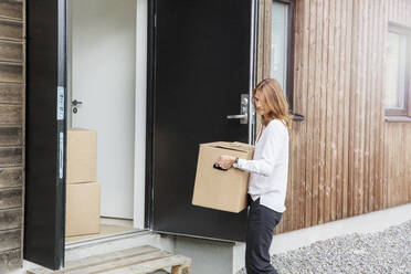 Woman carrying cardboard box into house - FOLF10457