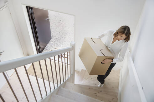 Woman carrying cardboard box up staircase - FOLF10458