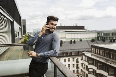 Junger Mann spricht auf dem Balkon mit einem Handy - FOLF10519