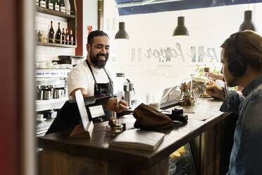 Lächelnder Barista bedient jungen Mann im Café - FOLF10600