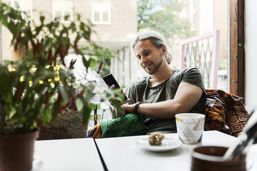 Junger Mann mit Smartphone im Cafe - FOLF10608