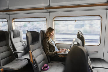 Junge Pendlerin im Zug mit Laptop - FOLF10654