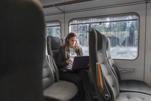 Junge Pendlerin im Zug mit Laptop - FOLF10657