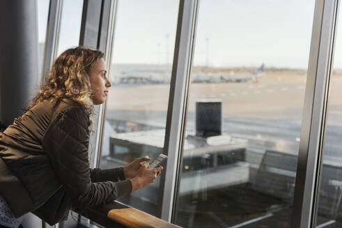 Frau mit Smartphone am Flughafenfenster - FOLF10662