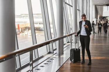 Frau mit Koffer und Smartphone im Flughafen - FOLF10668