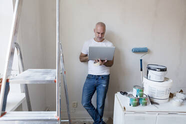 Mid adult man looking at laptop during apartment renovation - FOLF10691