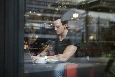 Young man using laptop behind window - FOLF10757