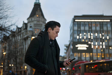 Young man holding cell phone walking down city street - FOLF10765