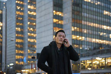 Young man talking on cell phone walking down city street - FOLF10766