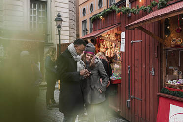 Ehepaar schaut auf dem Weihnachtsmarkt auf ein Handy - FOLF10771