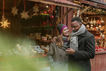 Ehepaar schaut auf dem Weihnachtsmarkt auf ein Handy - FOLF10772