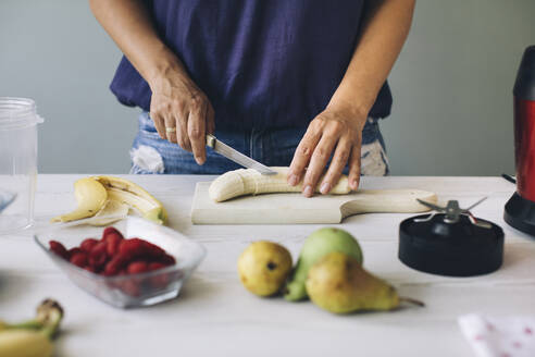 Woman cutting banana for a smoothie - MOMF00751