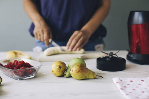 Woman cutting banana for a smoothie - MOMF00753