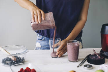 Frau gießt Smoothie in Gläser - MOMF00758