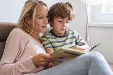 Mother and son reading a book together on couch at home - DIGF08132