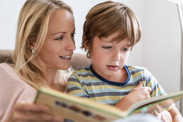 Mutter und Sohn lesen zusammen ein Buch auf der Couch zu Hause - DIGF08134