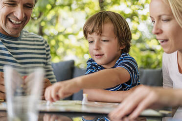 Glückliche Eltern und Sohn spielen ein Brettspiel auf der Terrasse - DIGF08136