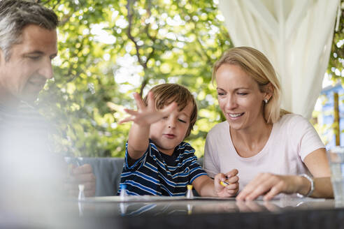 Glückliche Eltern und Sohn spielen ein Brettspiel auf der Terrasse - DIGF08137